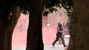 Un policía corre detrás de un grupo de manifestantes en medio de una nube de gas lacrimógeno en la capital de Túnez, el 25 de julio de 2021. En vídeo, imágenes de las protestas.