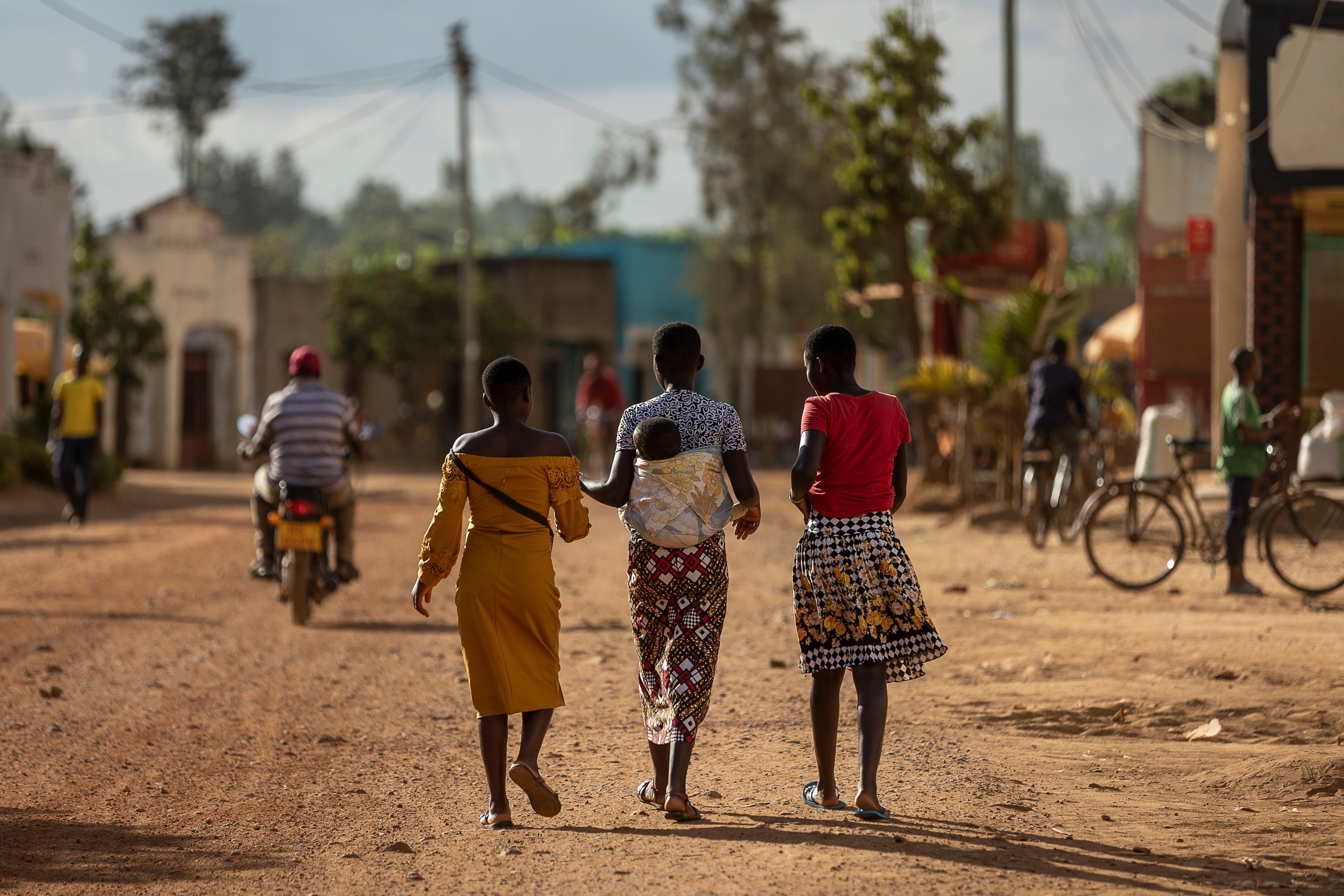 Tres jóvenes, una de ellas con su bebé en las espaldas, caminan por una calle del pueblo de Jurú, en Ruanda, en junio de 2023.