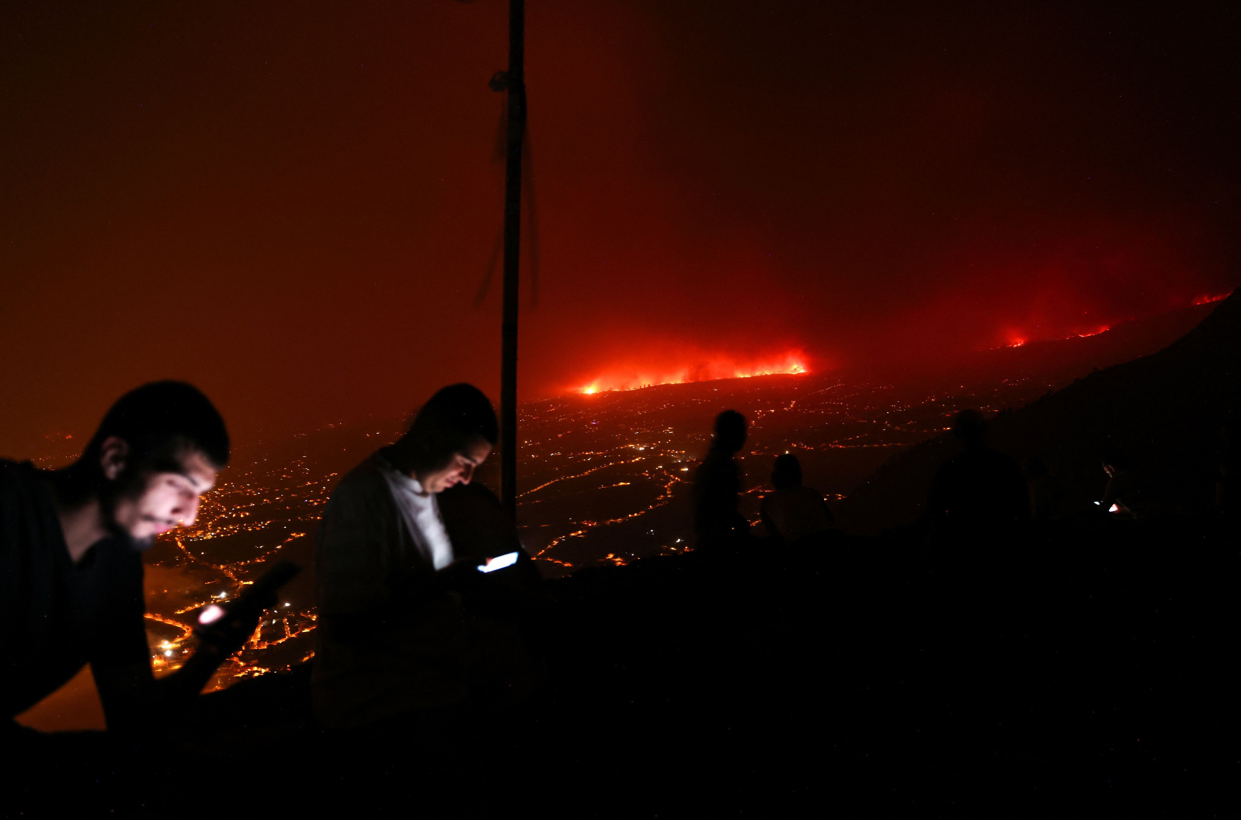 Dos jóvenes miran el móvil mientras prosigue el incendio, el sábado. 