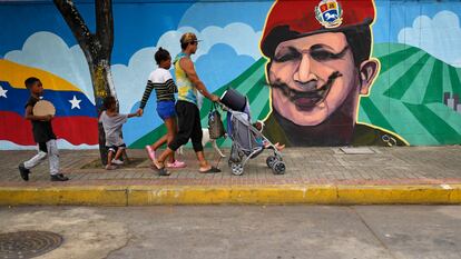 Una familia camina frente a un mural con el rostro del expresidente Hugo Chávez, este lunes en Caracas.
