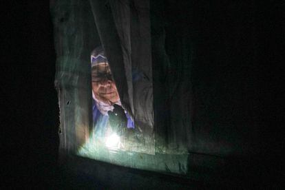 Una mujer se asoma por la ventana de su casa iluminada por la luz de una linterna en el sector seis de la Cañada Real Galiana, el mayor asentamiento irregular de Europa.