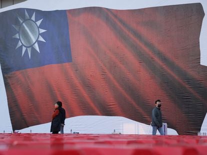 Un grupo de personas pasa junto a una imagen de una bandera taiwanesa durante un mitin de campaña del partido Kuomintang (KMT), en Taipéi, este viernes.