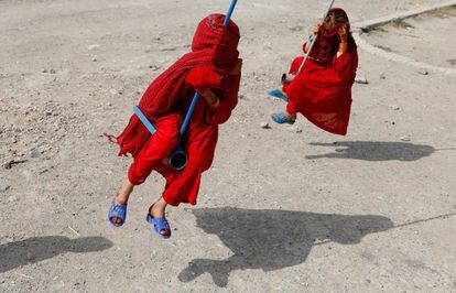 Afghan girls cover their faces while playing on swings in Kabul in 2019.