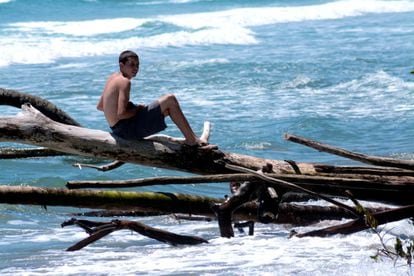 Un joven se sienta en uno de los trocos de los árboles que han sido derribados por el mar.