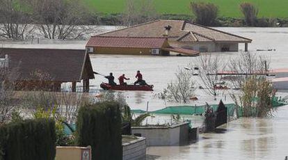 Varias personas a bordo de una lancha inspeccionan viviendas inundadas por la lluvia cerca del aeropuerto de Córdoba.