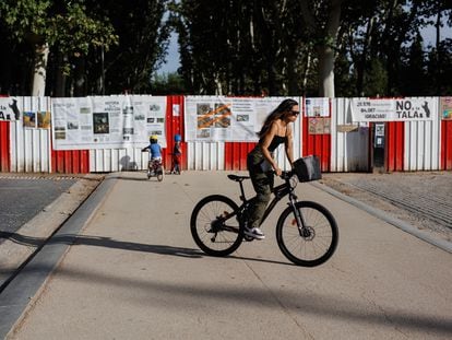 Una mujer pasa junto a unos carteles colocados por los vecinos del distrito de Arganzuela , a manera de protesta, en una de las vallas puestas en el parque Madrid Río, donde se proyecta una de las estaciones de metro de la ampliación de la línea 11, el 27 de septiembre de 2023.