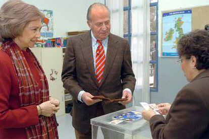 El rey Juan Carlos, junto a la reina Sofía, entrega su carné de identidad antes de votar en el colegio Monte del Pardo de Madrid.
