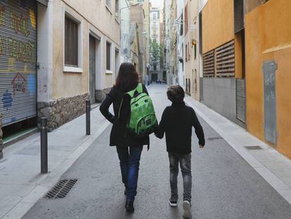 Una madre carga con la mochila de su hijo camino de la escuela.