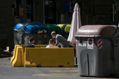 La terraza de un bar en pleno chaflán de la calle Aragón, entre contenedores de basura y reciclaje.