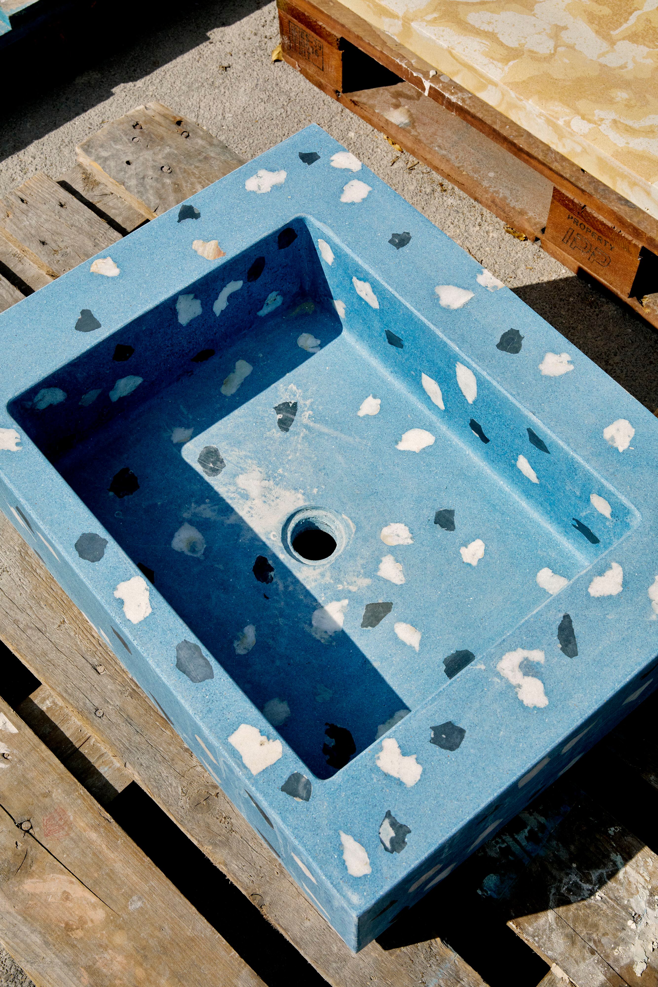 Lavabo de terrazo, cuya elaboración implica ir echando la mezcla pigmentada en azul en un molde mientras los áridos (los fragmentos grandes) se van colocando manualmente capa a capa.