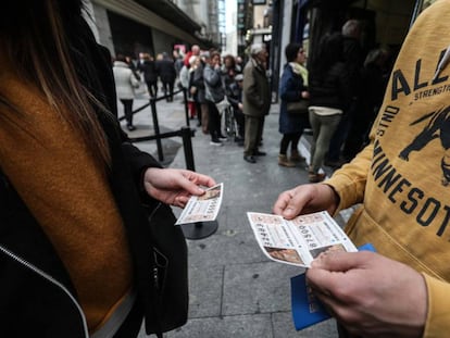 Dos personas estudian sus décimos para el sorteo de el Niño en la calle del Carmen de Madrid, delante de la cola de Doña Manolita.