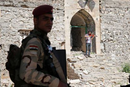Un militar hace guardia en unas ruinas en Mosul. De fondo, un violinista que vivi&oacute; bajo el r&eacute;gimen del ISIS toca una pieza.