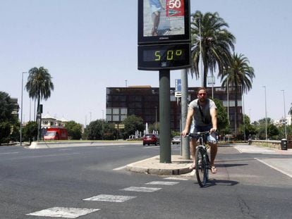 Un joven pasa con su bicicleta junto a un termómetro que marca 50 grados en Córdoba.