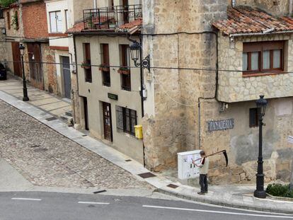 Un hombre con guadaña pasa por delante de una panadería en Frías (Burgos).