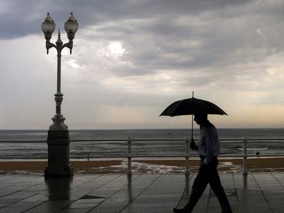 Un hombre se protege con el paraguas de la lluvia, en el paseo de muro de la playa de San Lorenzo de Gijón, el pasado 29 de agosto.