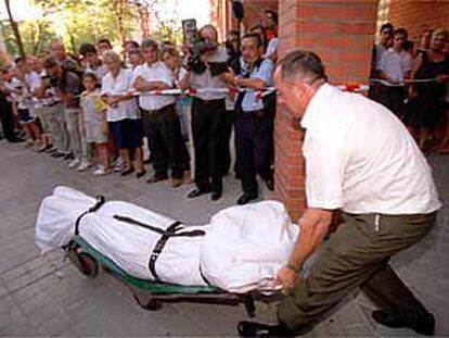 Los vecinos observan mientras un empleado de la funeraria saca de la vivienda de vallecas el cadáver de una de las mujeres tiroteadas.