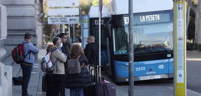 Varias personas esperan el autobús en una parada de la EMT en Cibeles, en Madrid. 