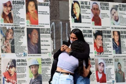 Dos mujeres se abrazan delante de imágenes de personas desaparecidas, en Guadalajara, Jalisco, este domingo.
