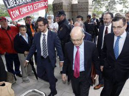 El ministro de Hacienda, Cristóbal Montoro, pasa junto a un un grupo de afectados por las preferentes que se concentraron a la entrada de la Universidad Internacional Menéndez Pelayo donde hoy se celebró el seminario " Competitividad y Marca España ".
