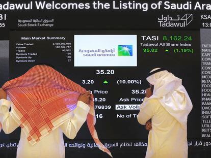 Dos hombres observan un panel de cotización de Saudi Aramco en la Bolsa de Riad.