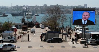 Una pantalla con una emisi&oacute;n de Vlad&iacute;mir Putin destaca sobre un puerto de Sevastopol, en Crimea.