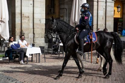 Un policía municipal a caballo pasa delante de los clientes de una terraza en la Plaza Mayor, sin mascarilla, pese a ser obligatorio. 