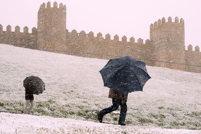 Dos personas se protegen de la nieve junto a la muralla de Ávila, este miércoles. En plena primavera la nieve ha regresado a amplias zonas de la península en una cota entre 900 y 1.000 metros, acompañada de un acusado descenso térmico generalizado, con máximas que, en apenas 24 horas, se han desplomado de forma notable -entre 6 y 9 grados- e incluso extraordinaria, hasta 14 grados. 
