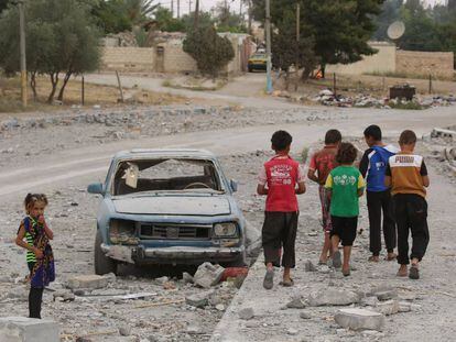 Hasan (de rojo) y sus amigos pasan junto a un coche destrozado en la ciudad siria de Al-Tabqa, en mayo de 2017. Hasan y su familia han tenido que cambiar de ciudad dos veces debido a la violencia, lo que le obligó a dejar la escuela en el grado 3.   