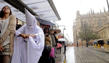 Un nazareno de la hermandad de la Paz exprime su túnica bajo una marquesina protegiéndose de la lluvia que ha deslucido las primeras procesiones del Domingo de Ramos de Sevilla, 24 de marzo de 2013.