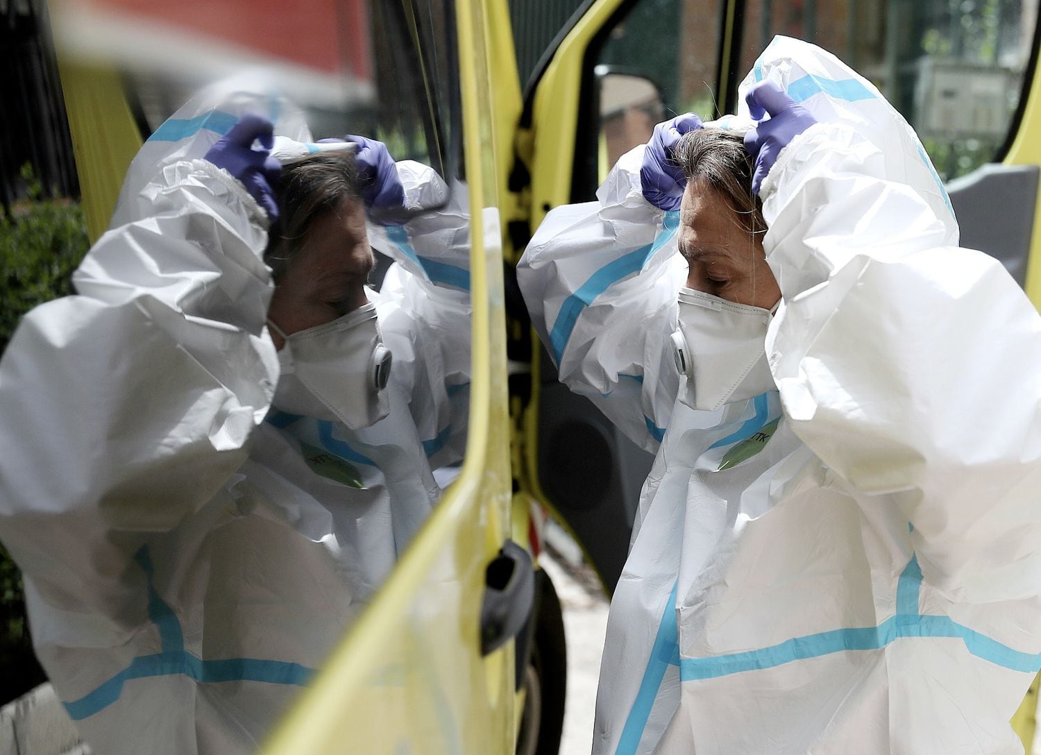 La médica se coloca el traje con el cristal de la ambulancia como ayuda, momentos antes de entrar en un domicilio, en Madrid.