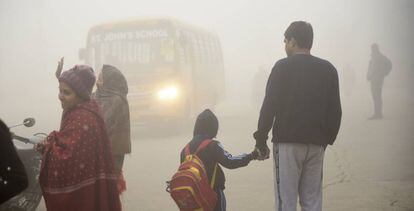Un niño y su padre esperan el autobús del colegio en Nueva Delhi, entre la polución causado por el polvo, las emisiones de las fábricas y la quema de carbón y basura para calentarse en invierno.