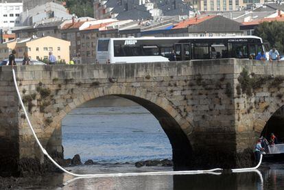 Varios agentes colocan barreras para frenar la mancha de combustible a la altura del puente romano de O Burgo.