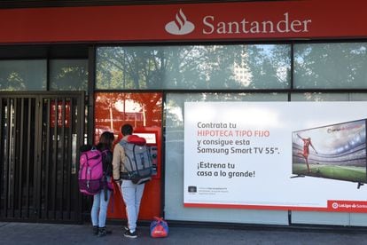 Dos personas retiran dinero de un cajero automático junto a un anuncio de hipotecas del Banco Santander, en una oficina de Madrid.