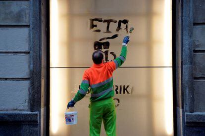 Un trabajador municipal limpia una pintada en una pared en una calle de Bilbao en la que se lee 
