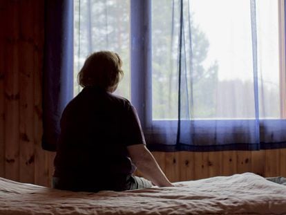 Una mujer sentada en su cama frente a la ventana.