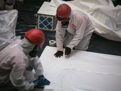 Operarios con equipos de protección trabajan en la retirada de pizarras con amianto, en Barcelona en 2019.