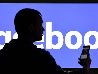 Un hombre con un smartphone junto a un logo de Facebook.