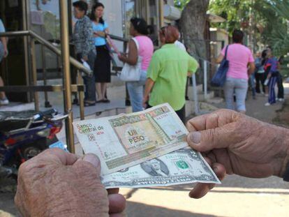 Un hombre muestra un peso convertible cubano y un dólar estadounidense frente a una oficina de la Western Union en La Habana (Cuba). 