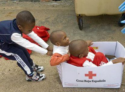 Tres de los niños rescatados de una patera en el Estrecho juegan con una caja de Cruz Roja.