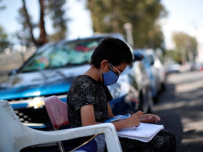 Un estudiante hace los deberes en la calle mientras su madre trabaja en un estacionamiento público, en Ciudad de México.