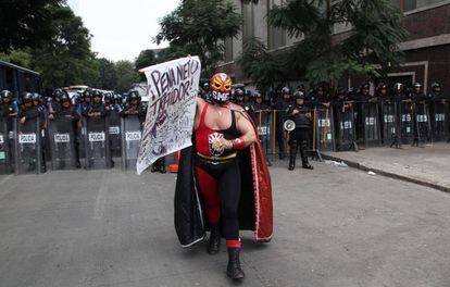 Un hombre vestido como luchador de lucha libre mexicana participa en la manifestación en contra de la reforma energética. Al fondo, un grupo de antidisturbios.