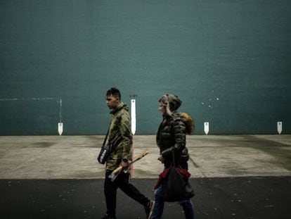 Dos personas caminan delante de un frontón con la bandera vasca, en Hernani.