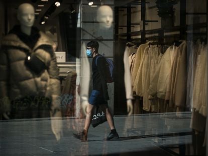 Reflejo en el escaparate de una tienda de un joven mientras camina con mascarilla por Portal de l'Àngel, en Barcelona.