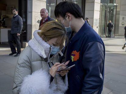 Una pareja asiática hace uso de su teléfono móvil en una calle de Londres durante la crisis del coronavirus.