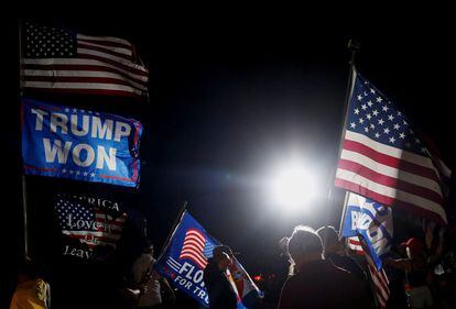 Los partidarios del expresidente de Estados Unidos, Donald Trump, sostienen banderas mientras se reúnen frente a su casa, el lunes.