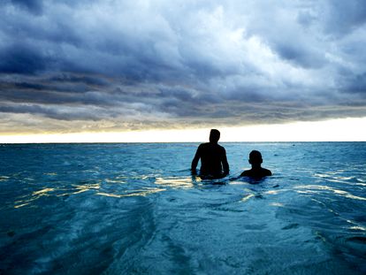 Dos hombres anónimos se bañan en una playa de Cuba bajo nubes de tormenta.