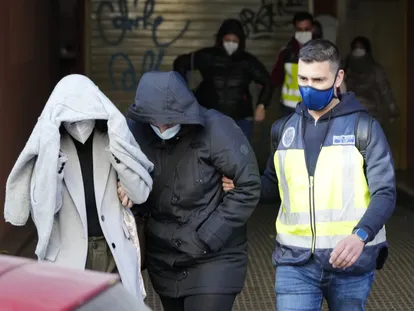 Un agente de la Policía Nacional acompaña a dos de los detenidos en la operación de este lunes en el Ayuntamiento de Cornellà.