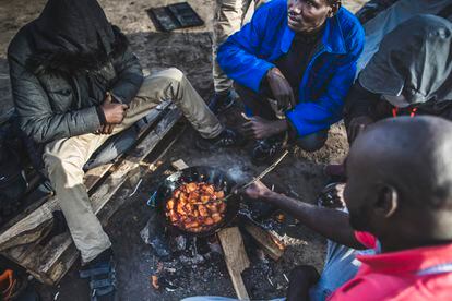 Un grupo de inmigrantes cocina y se calienta junto a un fuego en el campamento en el que aguardan para cruzar desde Calais, en Francia, hasta el Reino Unido