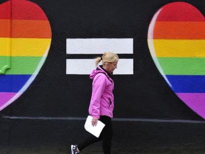 Una mujer camina junto a una pintada de dos corazones con los colores del arco&iacute;ris en Dubl&iacute;n.