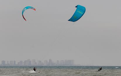 Dos personas practican kitesurf bajo un cielo plomizo en la Malvarrosa.